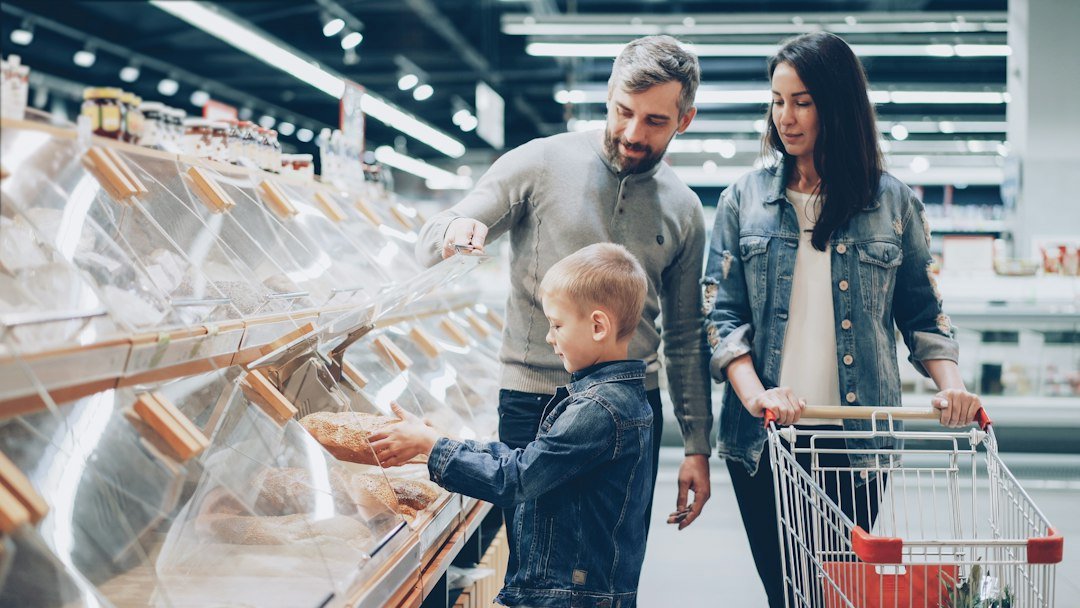 A young boy helps his parents choose bread at a grocery store bakery section while shopping together as a family.